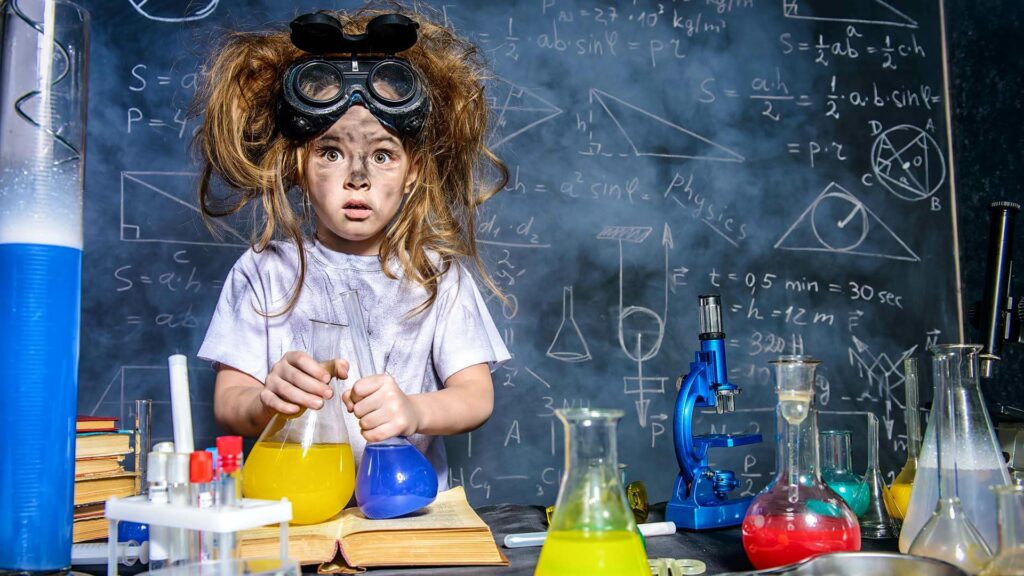 The image depicts a young child in a simulated science lab setting, surrounded by colorful laboratory equipment. The child wears oversized protective goggles pushed up on their head, and their hair is tousled, adding to the comical and exaggerated nature of the scene. They are pouring a yellow liquid from one flask into another, with a focused and somewhat perplexed expression on their face. Behind the child is a blackboard filled with various mathematical and scientific equations and diagrams, suggesting a complex and intellectual backdrop. The overall scene is playful and suggests a fun, if slightly chaotic, introduction to project risk.
